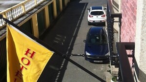 A hotel entrance with a yellow flag, a white car, and a blue car parked in front. - Hotel As Areas I (Viveiro)
