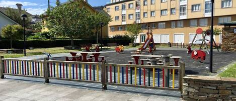 A playground with swings and slides, surrounded by a stone wall and a colorful fence.
