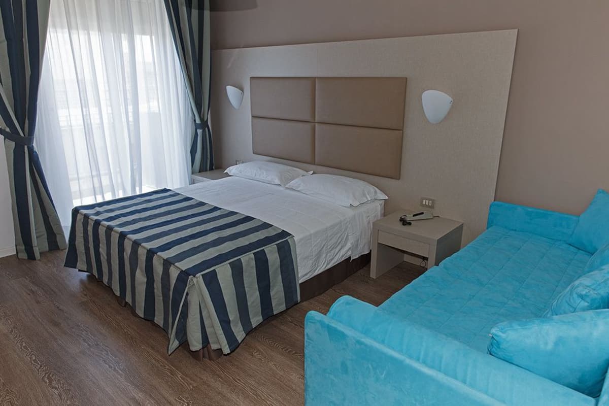 A hotel room with a bed, a bedside table, a chair, and a window with curtains.
