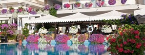 A hotel with a pool surrounded by potted plants and hanging flower arrangements. - Hotel Sirenetta (Jesolo)