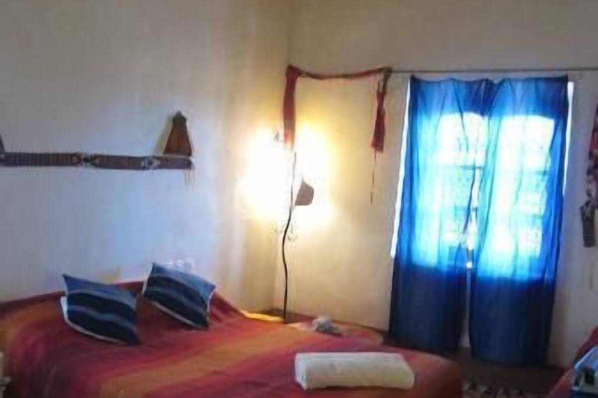 A room with two beds, a ceiling fan, a wall-mounted lamp, and a window with curtains.