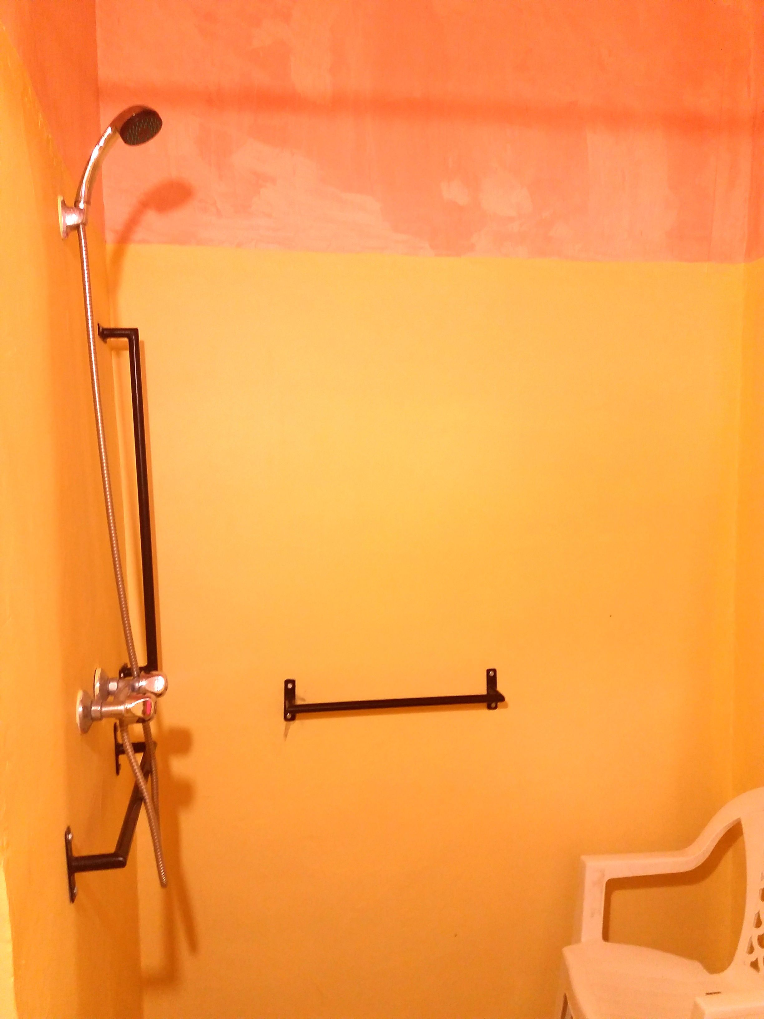 A bathroom with a shower, a towel rack, and a white chair.