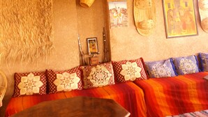A room with a wooden ceiling, a woven wall hanging, a sofa with patterned cushions, and a framed picture on the wall. - Dar Panorama (Skoura)