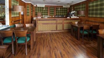 Una habitación con paneles de madera, una zona de bar central, sillas tapizadas en verde y suelo de madera.