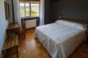 A bedroom with a wooden bed, a wooden desk, a chair, and a window with a view of buildings and trees. - Hotel As Areas II (Viveiro)