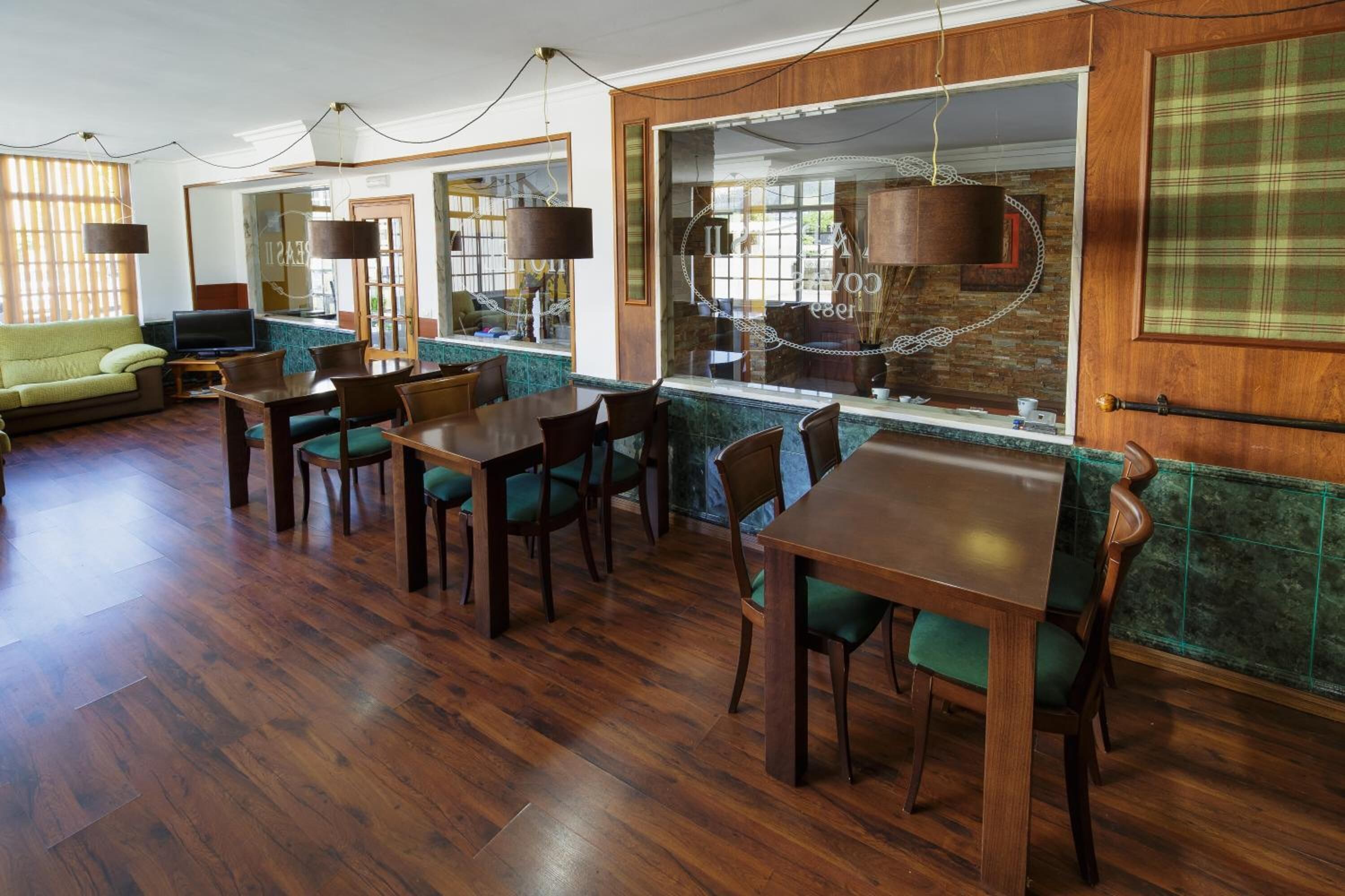 Una habitación amplia con suelo de madera, un sofá verde, una mesa de comedor con sillas y un gran ventanal con vistas a la ciudad.