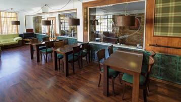 Una habitación amplia con suelo de madera, un sofá verde, una mesa de comedor con sillas y un gran ventanal con vistas a la ciudad.