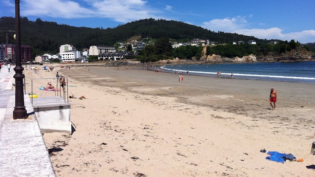 Una playa con un farol, orilla arenosa y edificios al fondo.