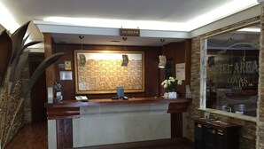Un mostrador de recepción con encimera de madera, un teléfono y un jarrón de flores. Un cartel sobre el mostrador dice 'RECEPCION'.