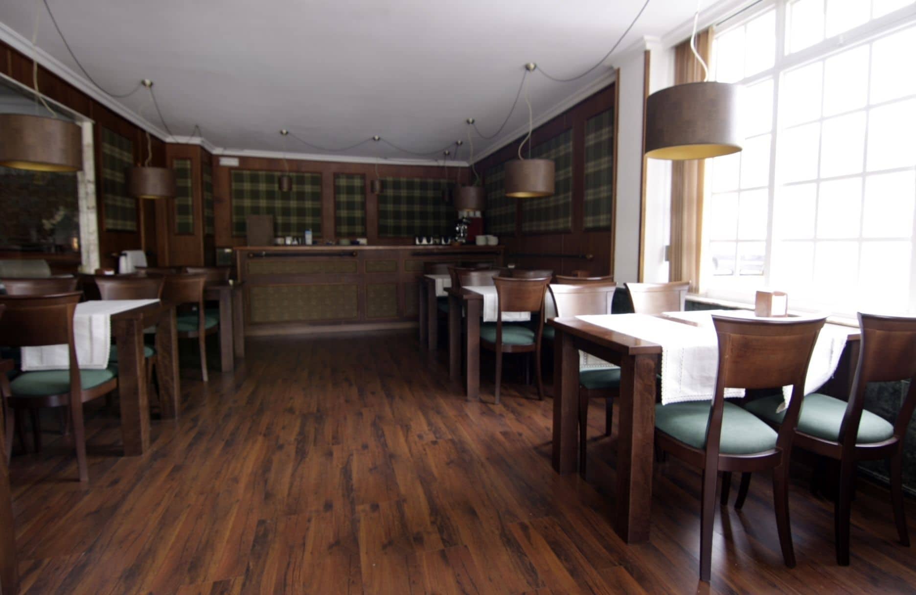 Un restaurante con piso de madera, sillas tapizadas en verde y una zona de bar.