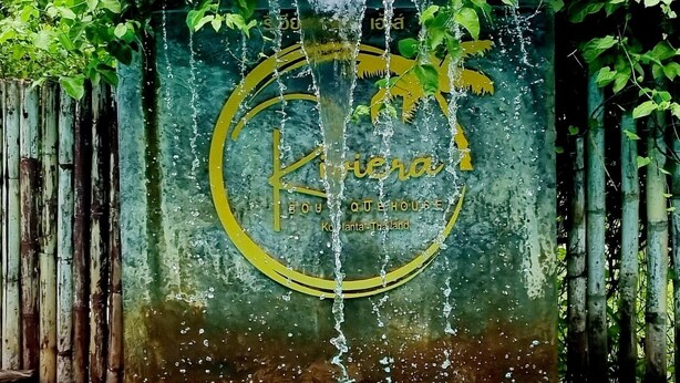 Une piscine dont l’un des murs est orné d’un logo et d’une inscription, et qui est entourée de verdure.