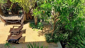 Un espace jardin aménagé avec un hamac, des chaises longues en bois et un escalier doté d’une rampe rouge.