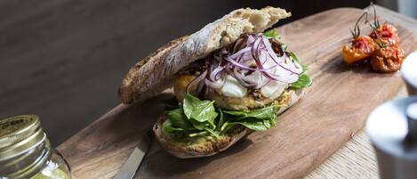 A sandwich on a wooden board with a knife and a jar of pickles nearby.