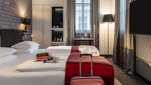Een hotelkamer met een bed, een rode koffer, een televisie, een bureau met een lamp en een boekenkast.