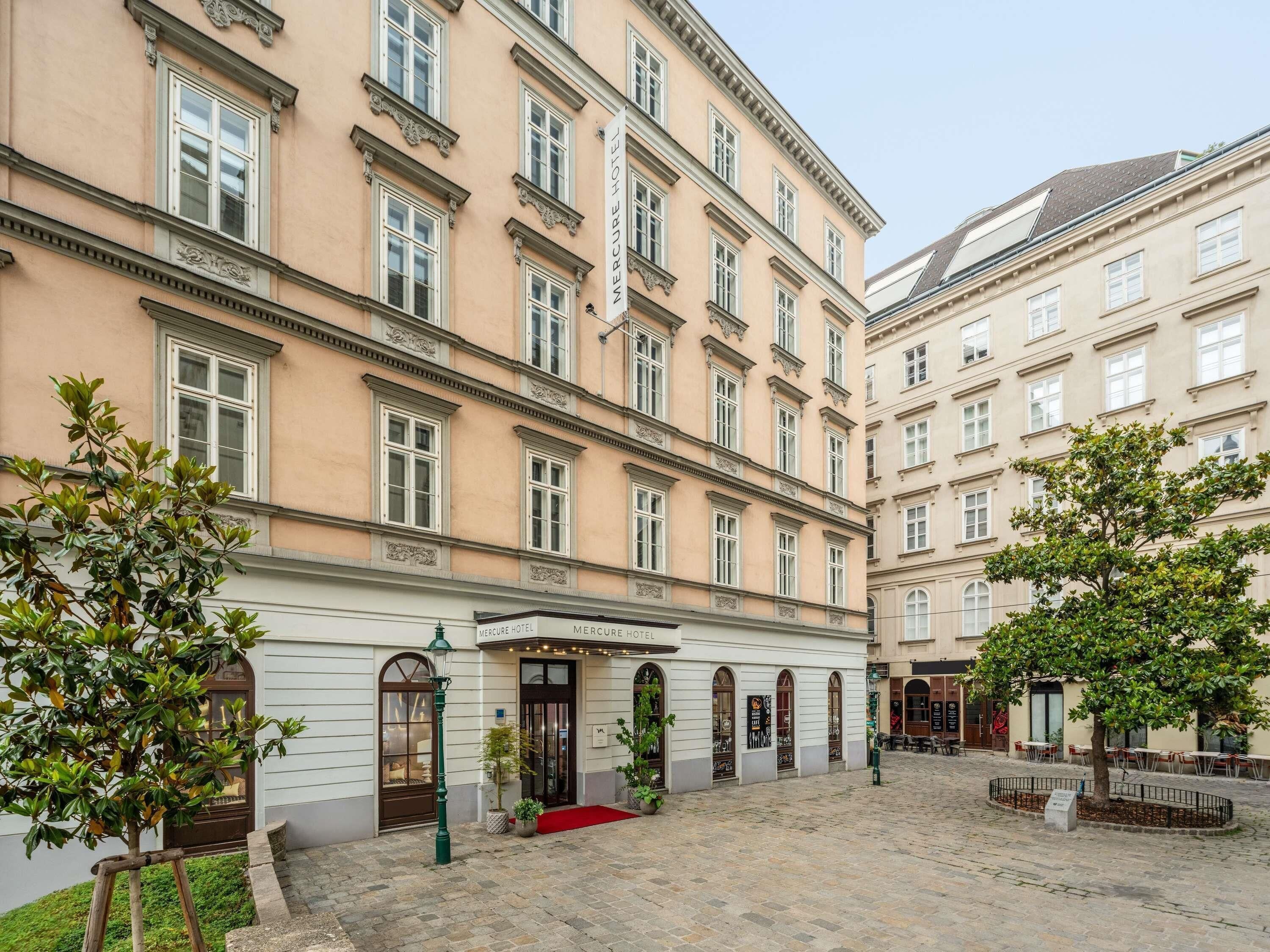 A historic building with a red carpet entrance, arched windows, and a courtyard with trees and outdoor seating.