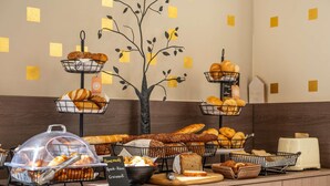 Een buffet met verschillende broden en gebak, een bordje dat huisgemaakte producten aangeeft, en een decoratieve wand met een ontwerp van een boom.