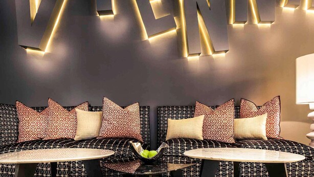 Een moderne zithoek met een bank, een kleine tafel en een muur met verlichte letters die 'VIENNA' vormen.