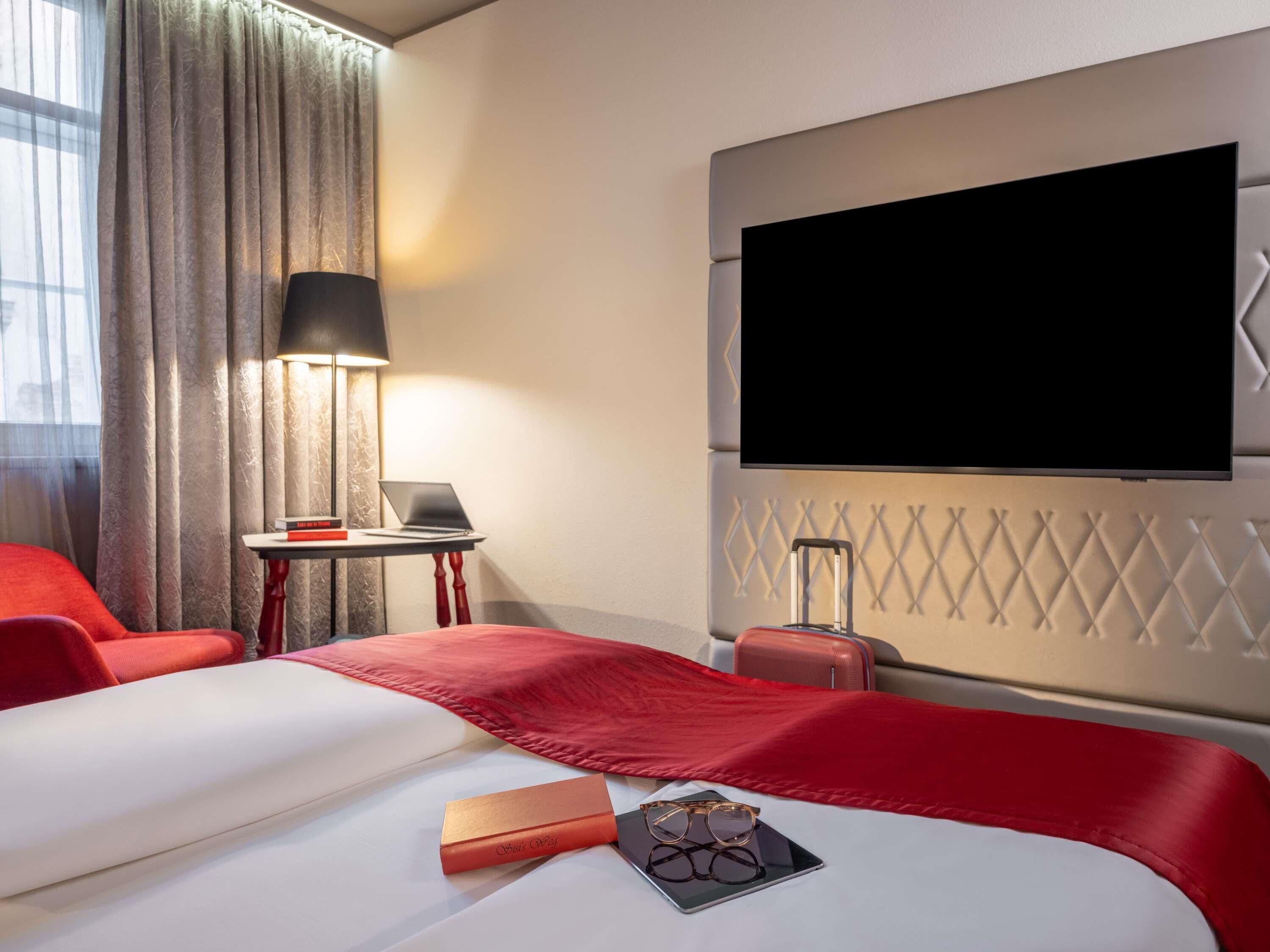 Une chambre d’hôtel avec deux lits, une télévision, un bureau avec un ordinateur portable et une valise.