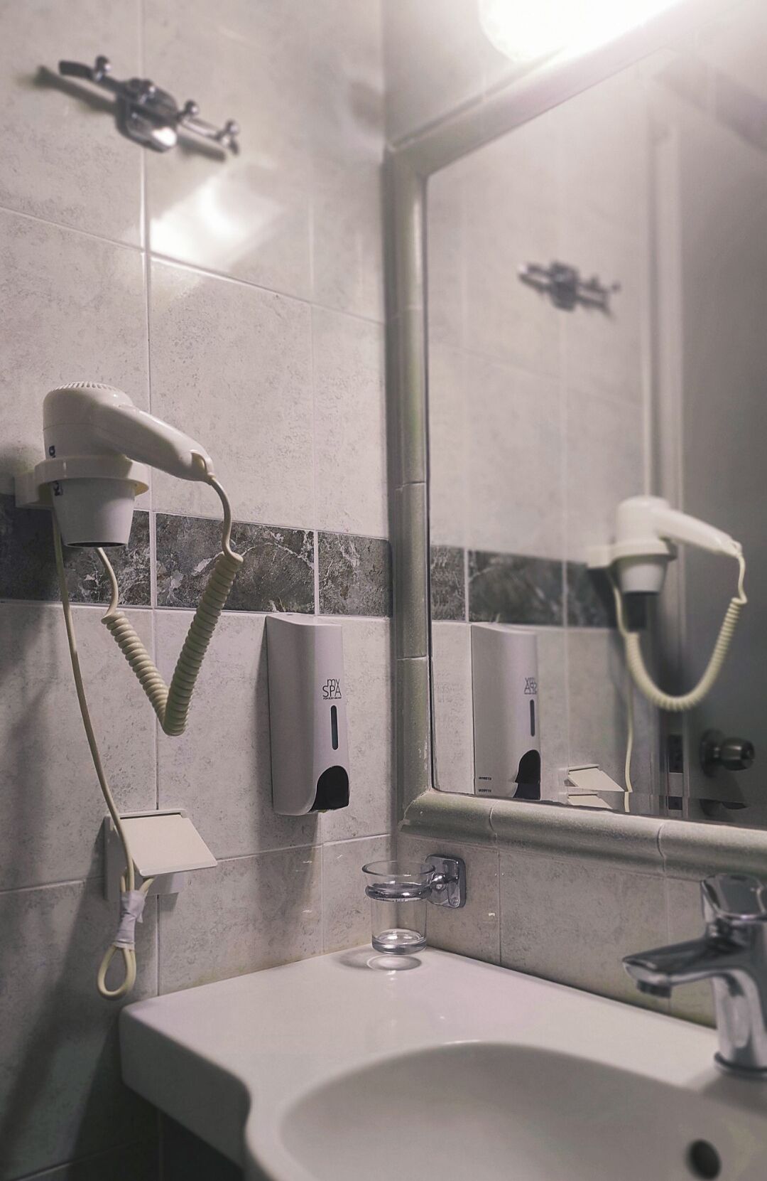 A bathroom with a sink, mirror, hairdryer, and hand dryer.