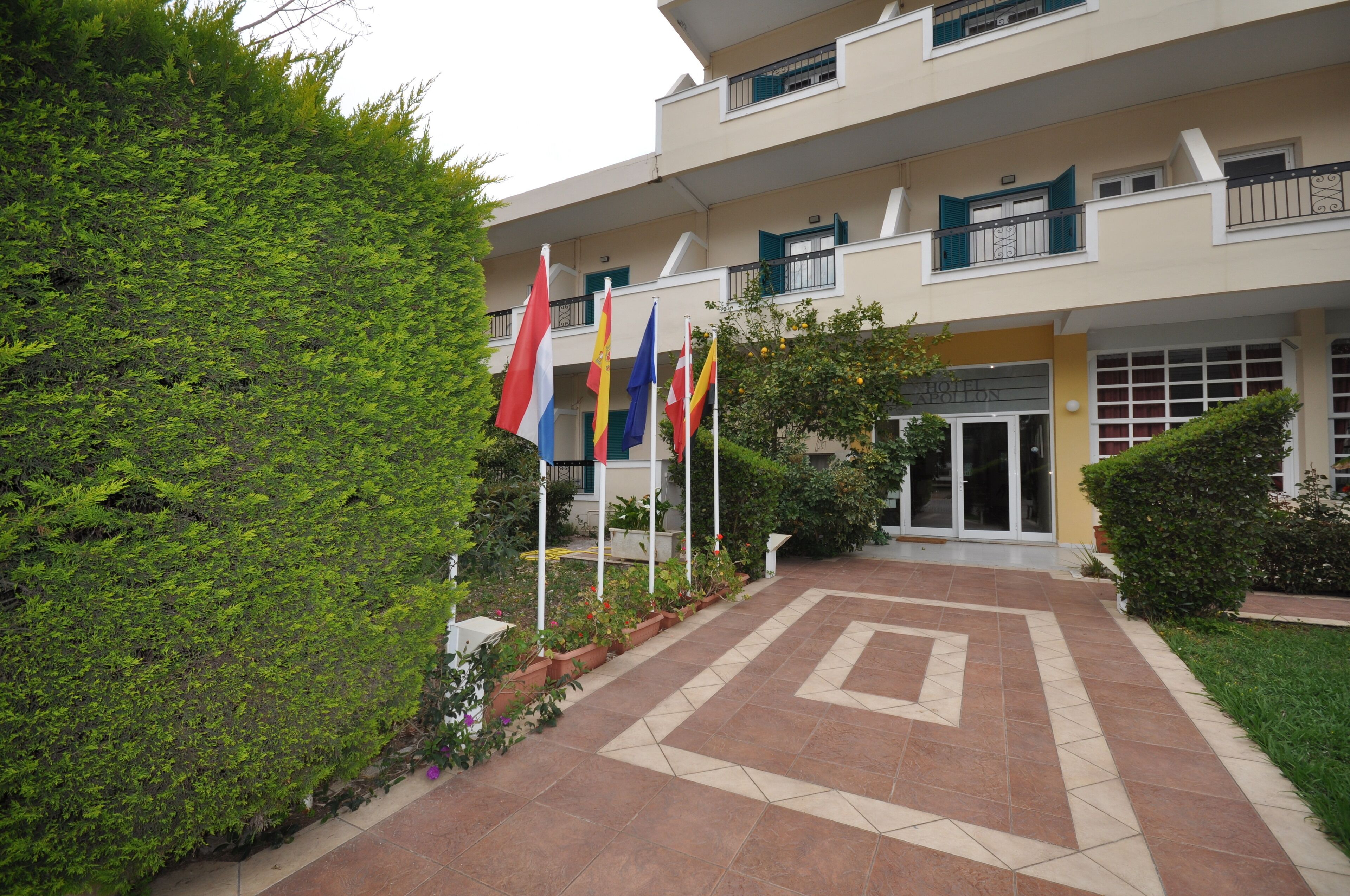A building with multiple flags, a tiled entrance, and a well-maintained garden.