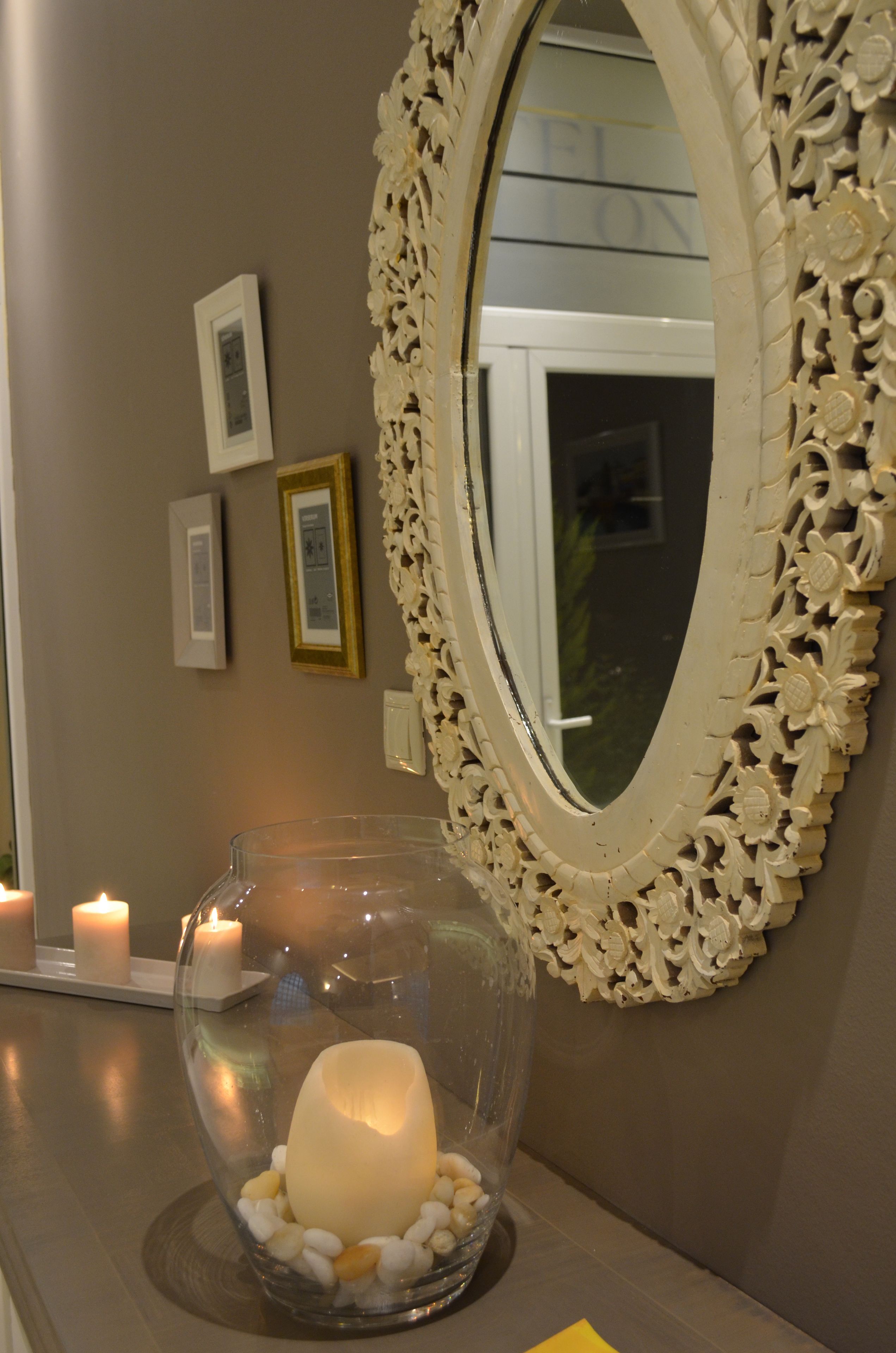 A mirror with an ornate frame, a glass bowl with a candle, and framed pictures on the wall.