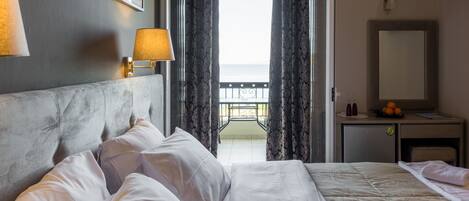 A hotel room with a bed, a bedside table with a lamp, a small desk with a mirror, and a view of the balcony.