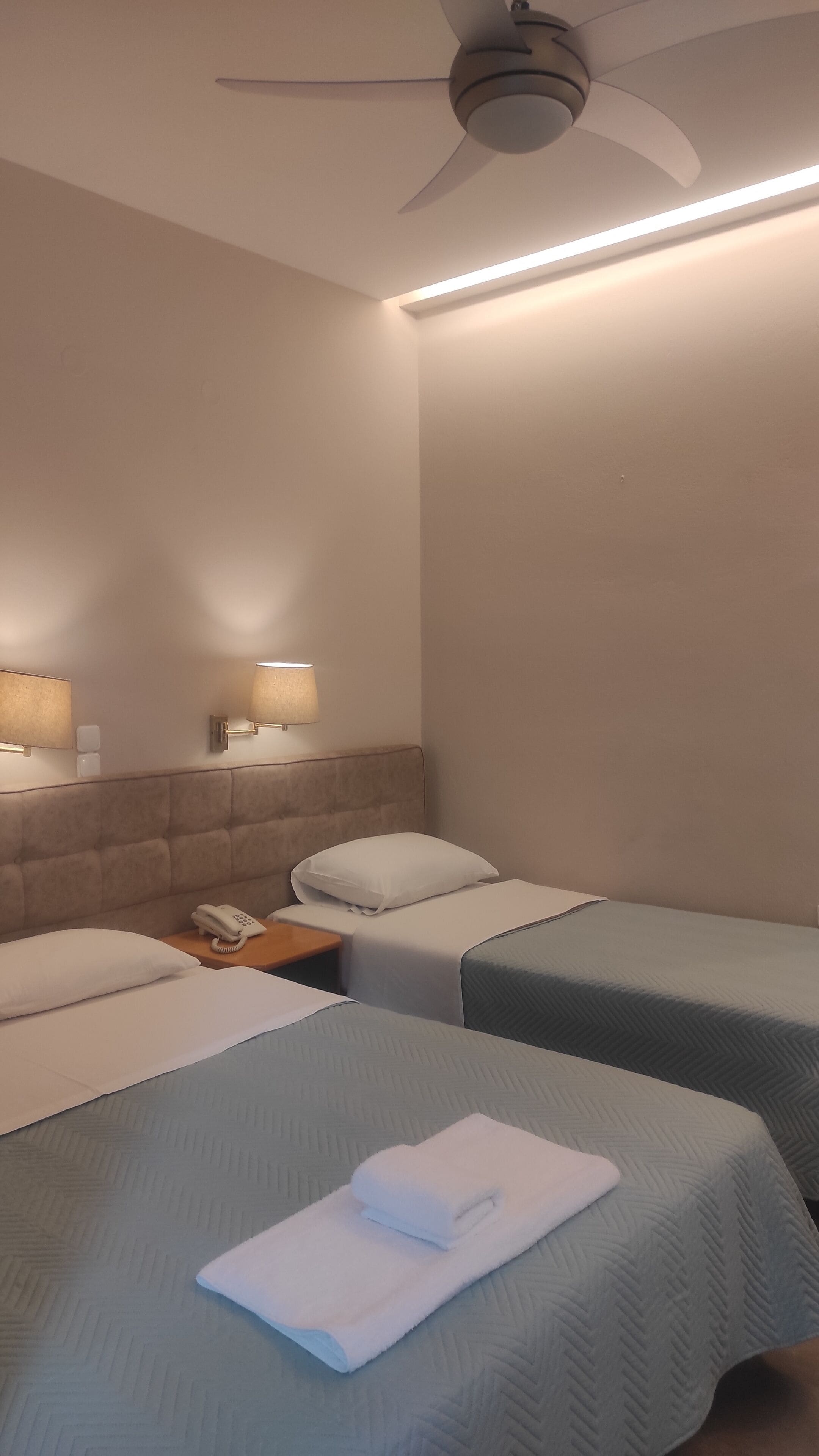 A hotel room with two beds, a ceiling fan, and wall-mounted lamps.