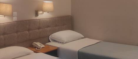 A hotel room with two beds, a ceiling fan, and wall-mounted lamps.