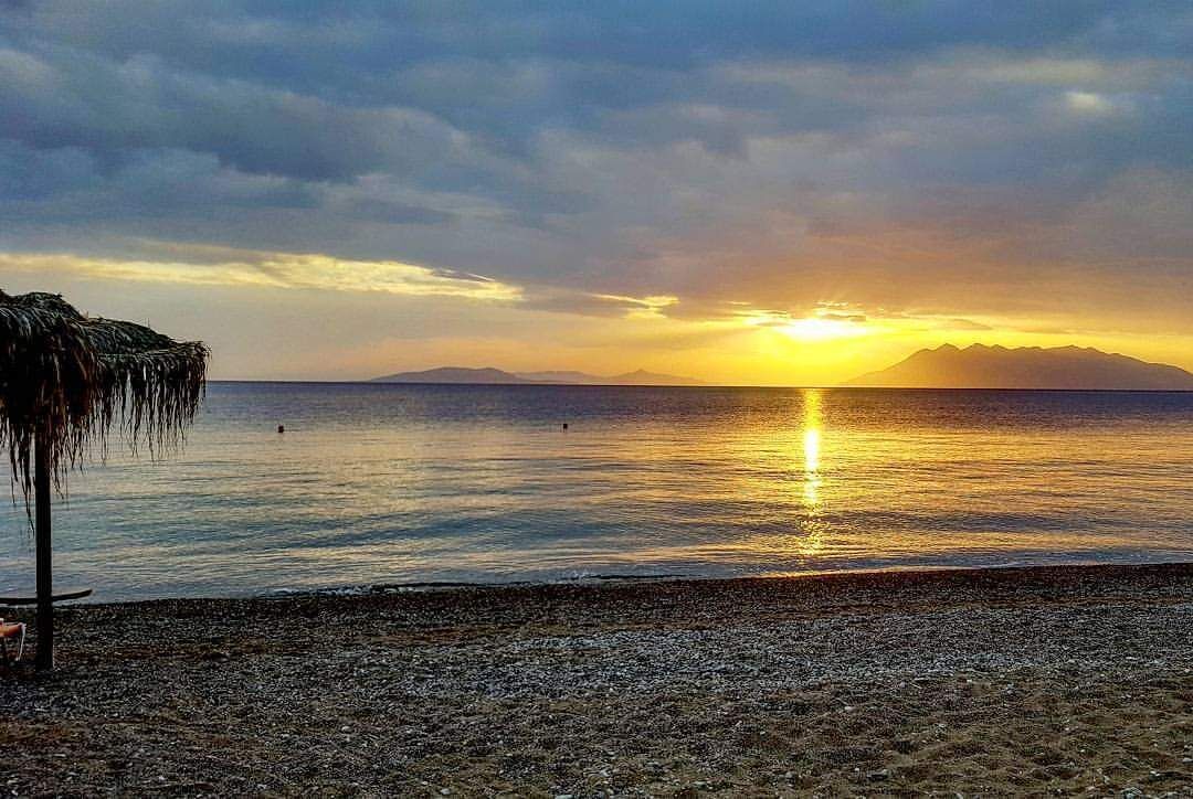 Una playa con una sombrilla de paja y una orilla pedregosa.