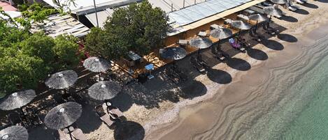 Vista aérea de un restaurante frente a la playa con mesas al aire libre y sombrillas.