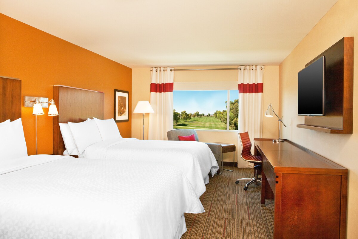 Habitación de hotel con dos camas, un escritorio, un televisor y vista a un campo de golf.