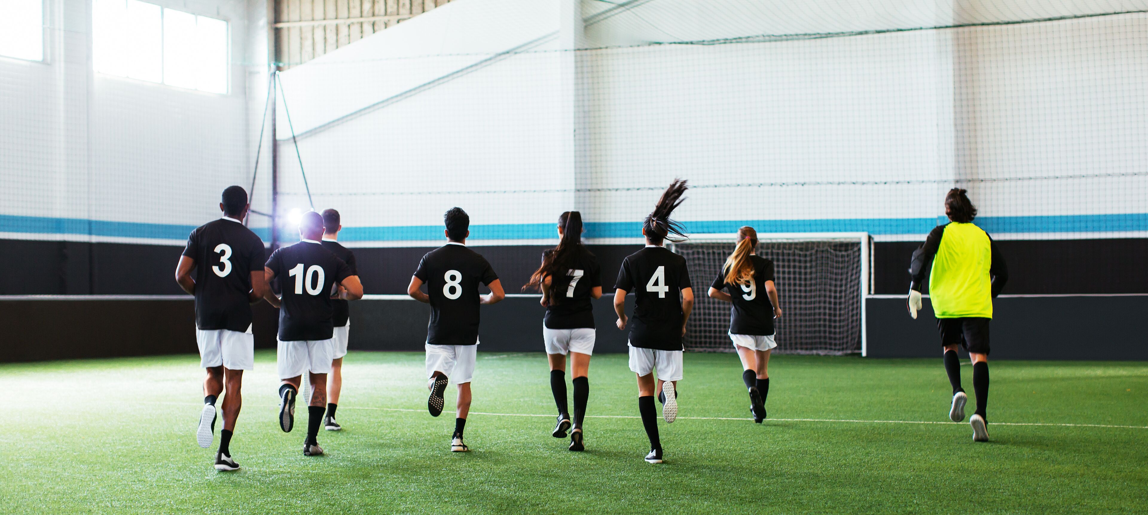 A group of people on a sports field, likely a soccer or volleyball court, with a net in the background.