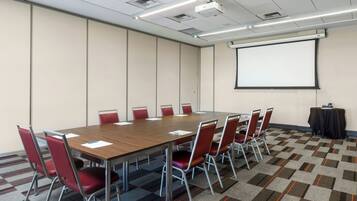 A conference room with a long table, red chairs, a projector screen, and a carpeted floor.
