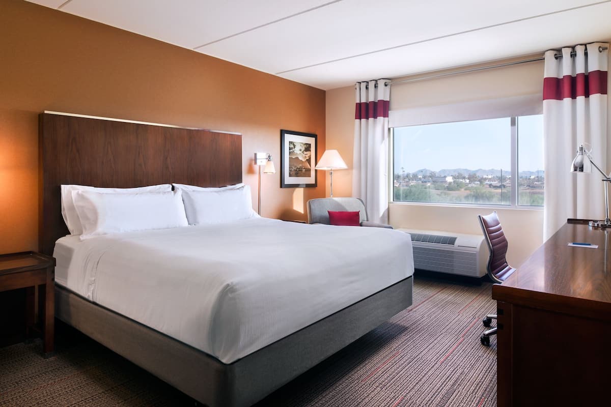 Habitación de hotel con una cama grande, un escritorio, una silla, una lámpara y vistas a la ciudad.