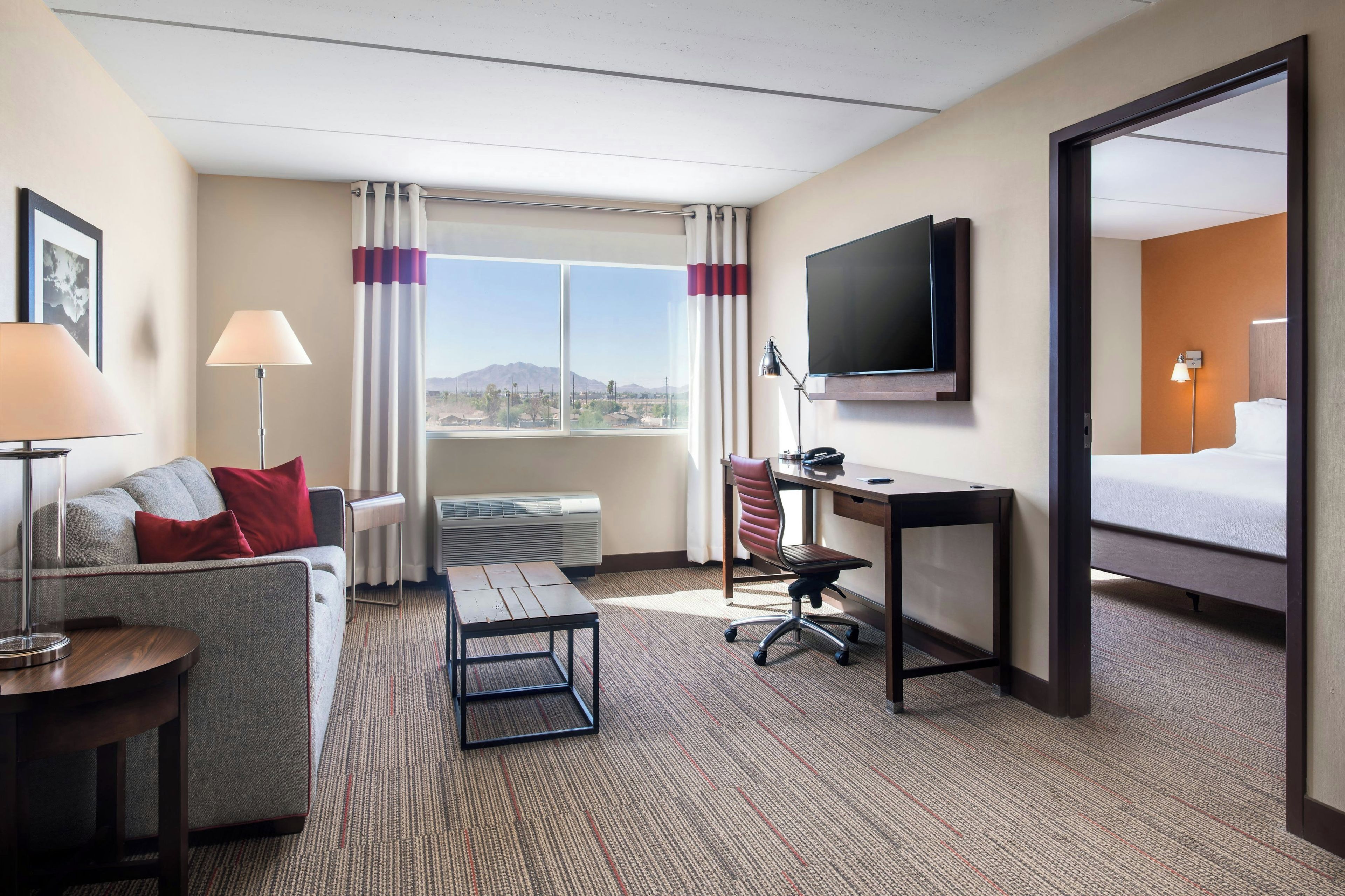 A hotel room with a bed, a desk, a chair, a TV, a sofa, a lamp, and a window with curtains.