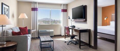 A hotel room with a bed, a desk, a chair, a TV, a sofa, a lamp, and a window with curtains.