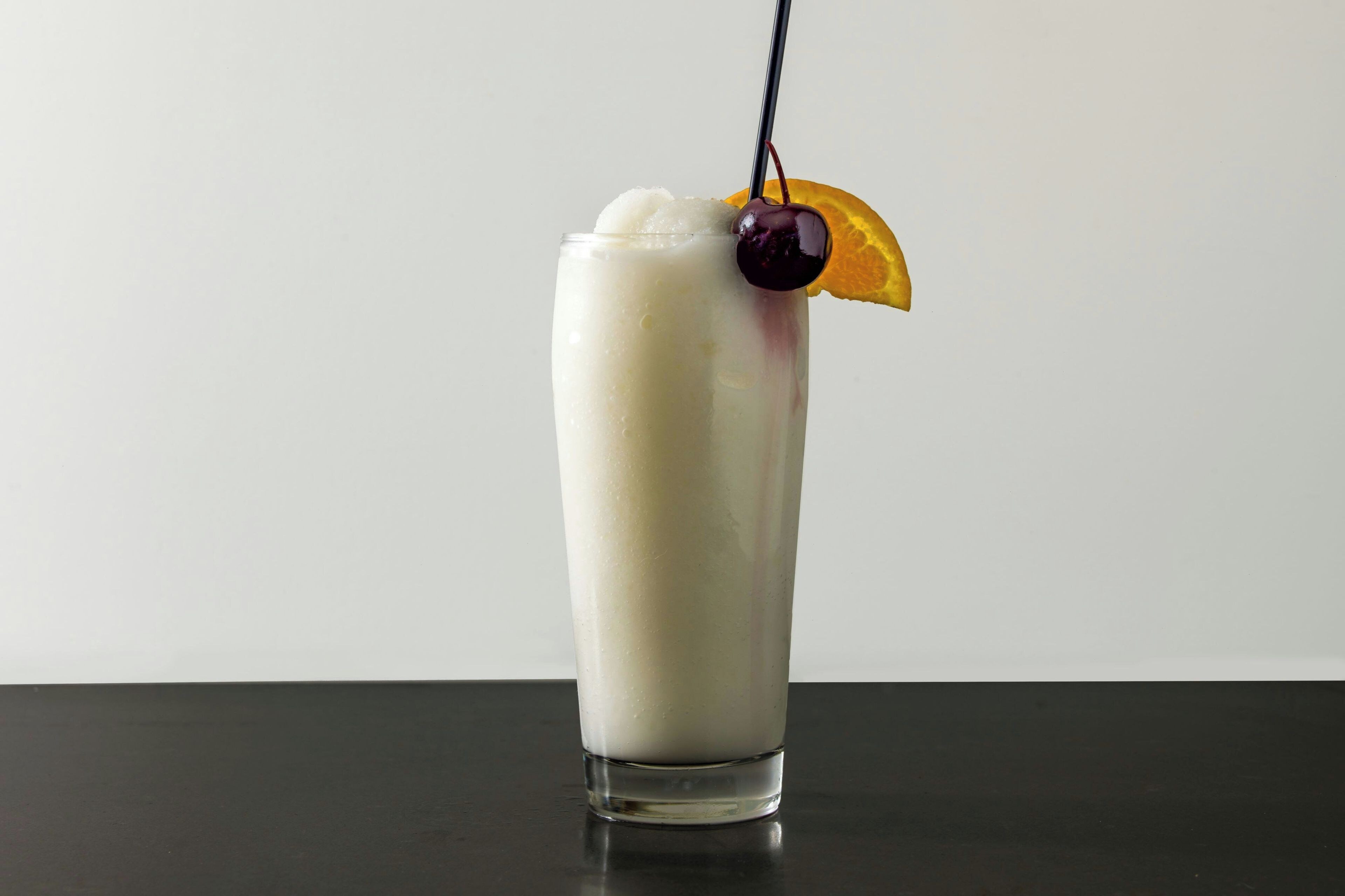 A tall glass with a creamy beverage, a cherry, and an orange slice garnish.