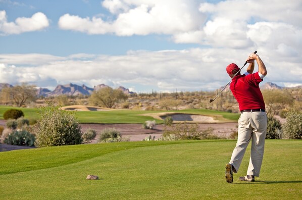 Un campo de golf con cielo despejado y montañas al fondo.