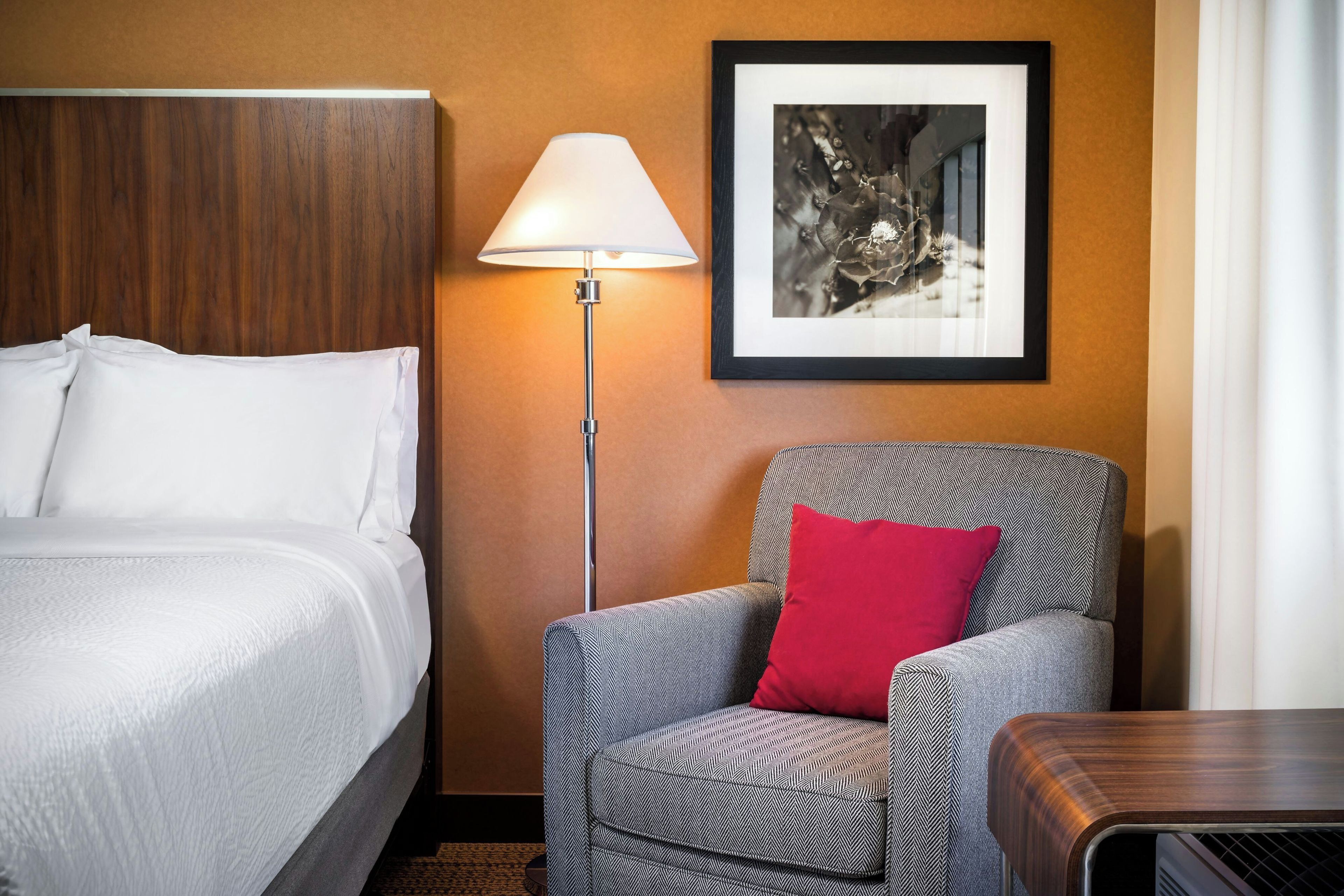 Une chambre d’hôtel avec un lit, une chaise dotée d’un coussin à motifs, une lampe sur pied et un tableau encadré accroché au mur.