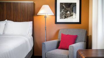 Une chambre d’hôtel avec un lit, une chaise dotée d’un coussin à motifs, une lampe sur pied et un tableau encadré accroché au mur.