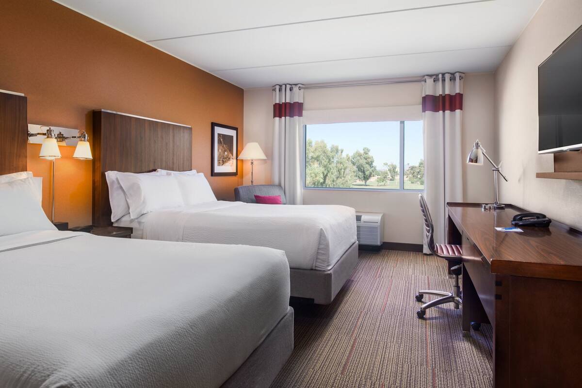 Una habitación de hotel con dos camas, un escritorio, una silla, un televisor y una ventana con cortinas.