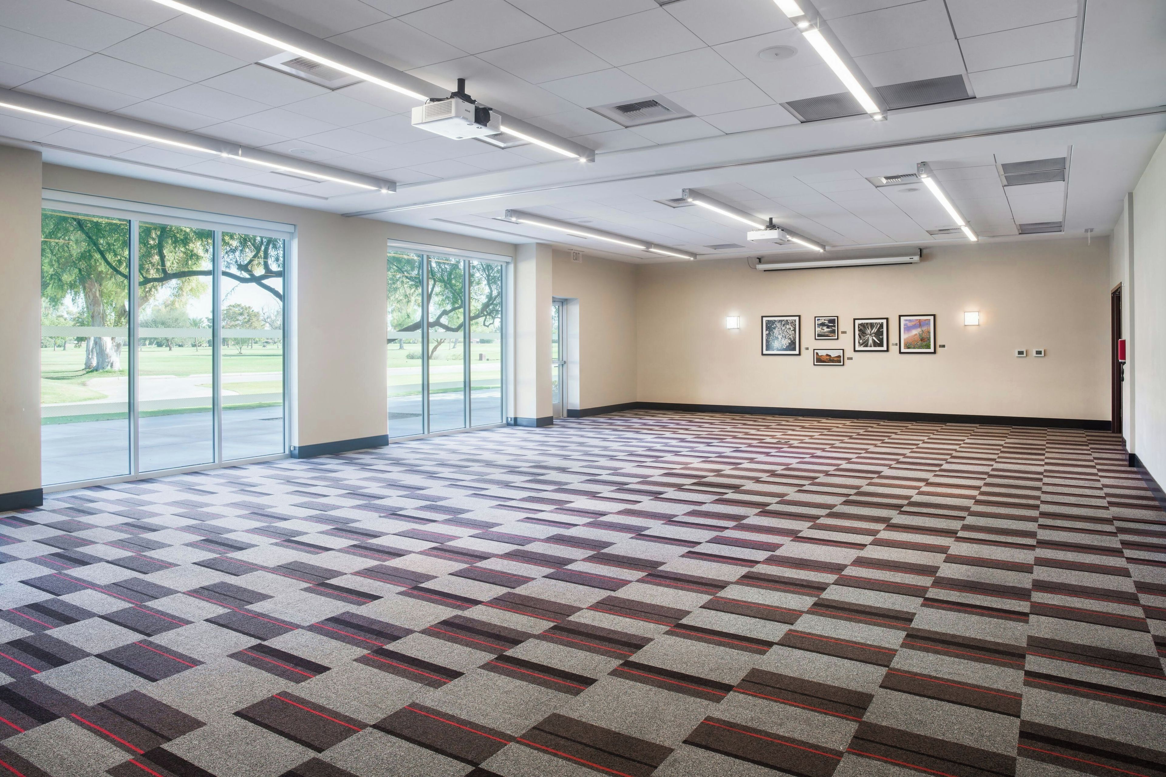 A spacious conference room with a patterned carpet, large windows, and a ceiling-mounted projector.