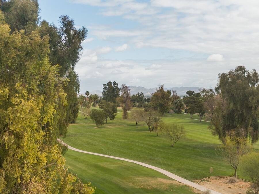 Un parcours de golf avec des allées bien définies, entouré d’arbres et bordé de montagnes lointaines.