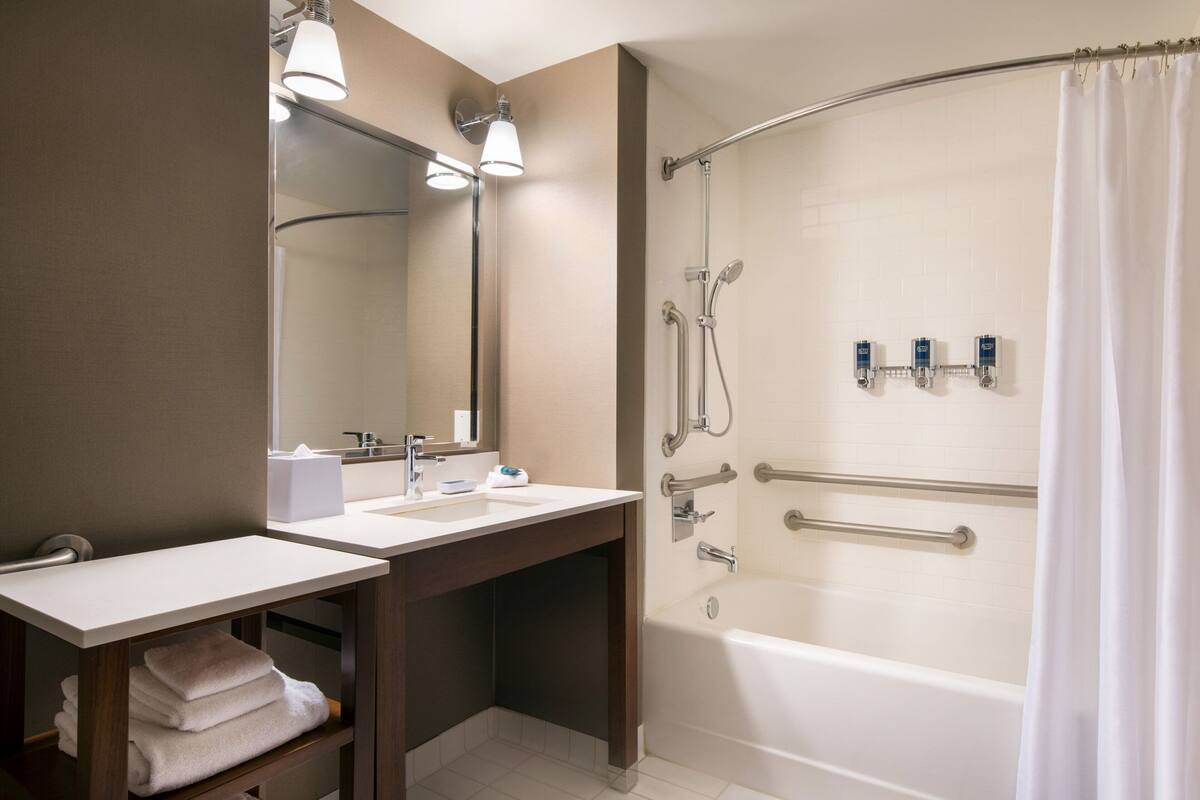 Un baño moderno con dos lavamanos, un espejo grande, una ducha con puerta curva y un perchero para toallas.