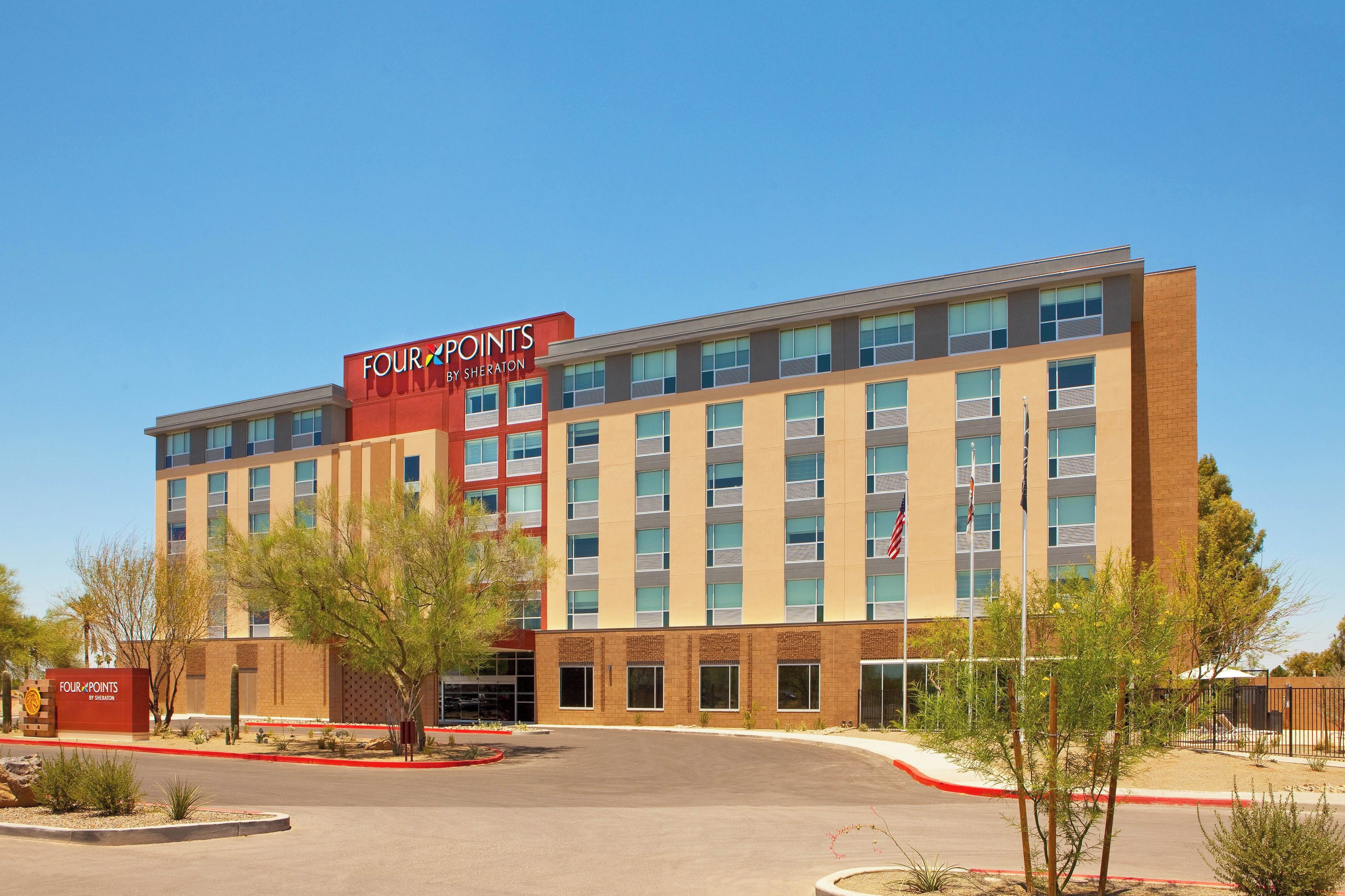 A multi-story hotel with a red and beige facade, large windows, and a parking lot with landscaping.