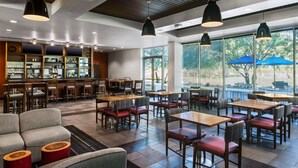 A modern restaurant with a bar area, multiple seating options including tables and chairs, and large windows offering a view of the outdoors.