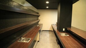 A modern restroom with dark wooden benches, stainless steel sinks, and a tiled backsplash. - Hotel Ross Morelia (Morelia)