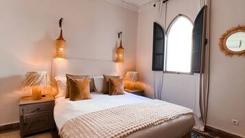 A bedroom with a large bed, two bedside lamps, a decorative mirror, and a window with curtains.