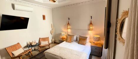 A bedroom with a large bed, two bedside tables, a TV mounted on the wall, and a ceiling light fixture.