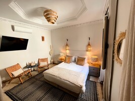 Un dormitorio con una cama grande, dos mesitas de noche, un televisor montado en la pared y una lámpara en el techo.
